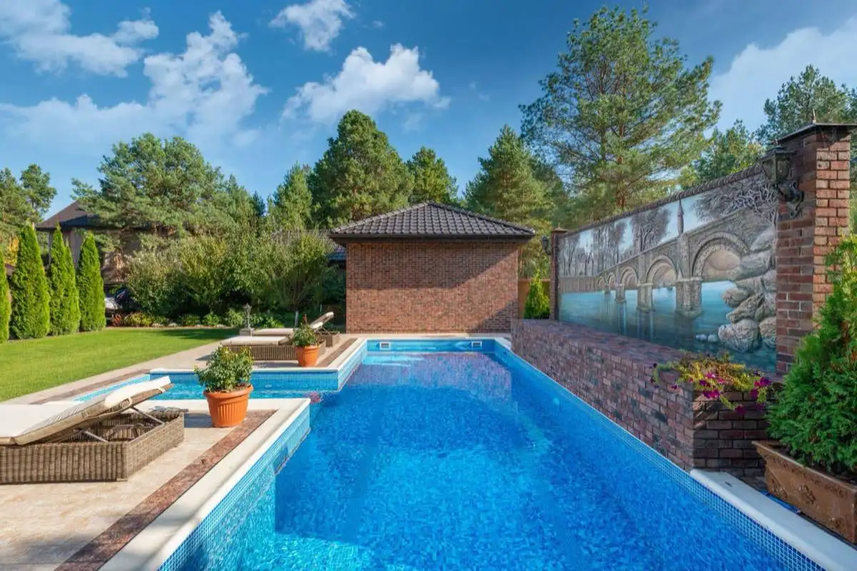 Inground swimming pool with tiled waterline and a brick surround in a landscaped backyard